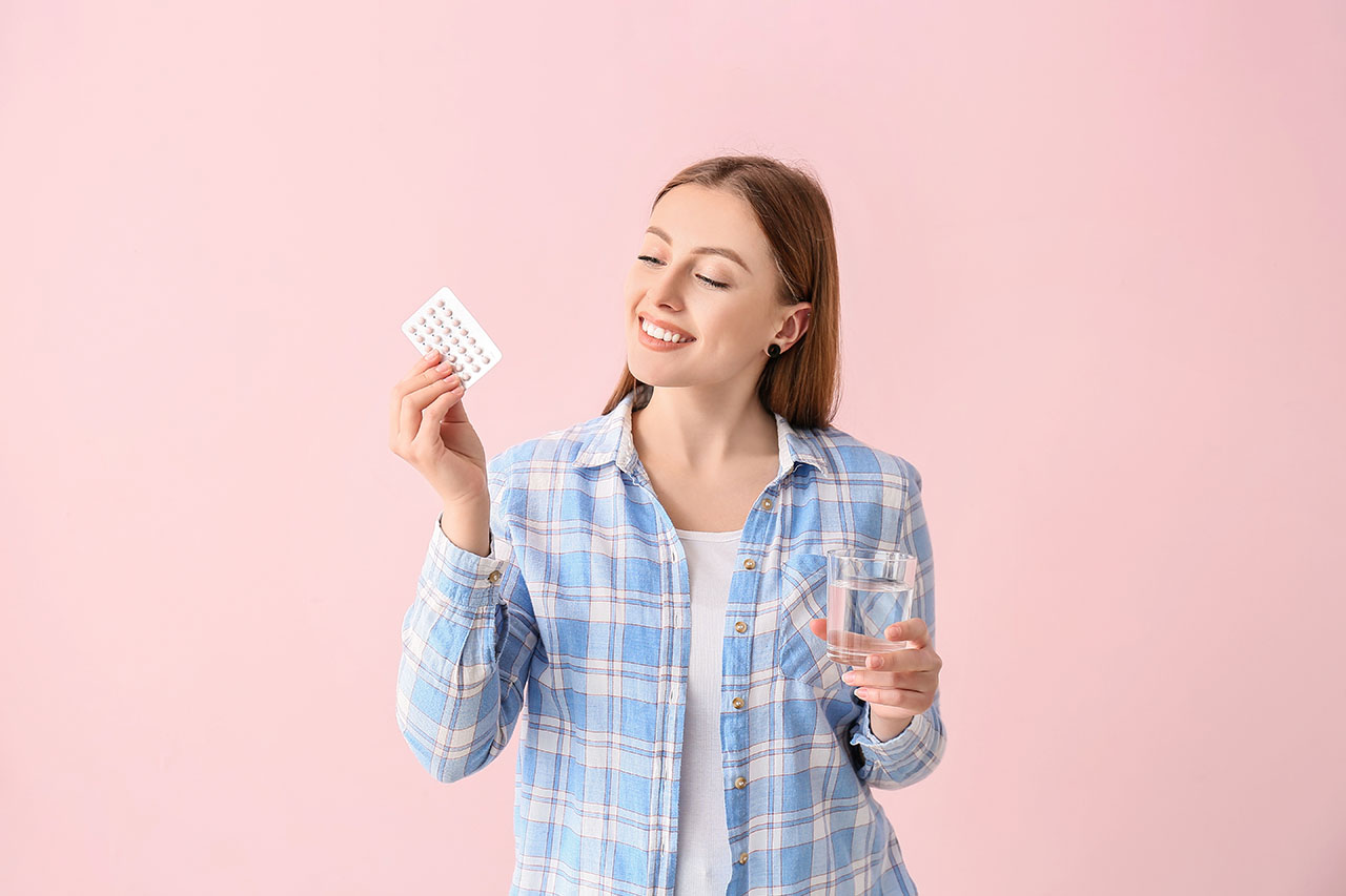 Young woman with birth control pills on color background