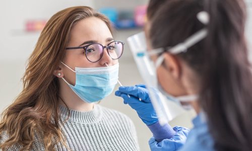 Female patient wearing mask over mouth is having sample taken from nose for a pcr test for covid 19